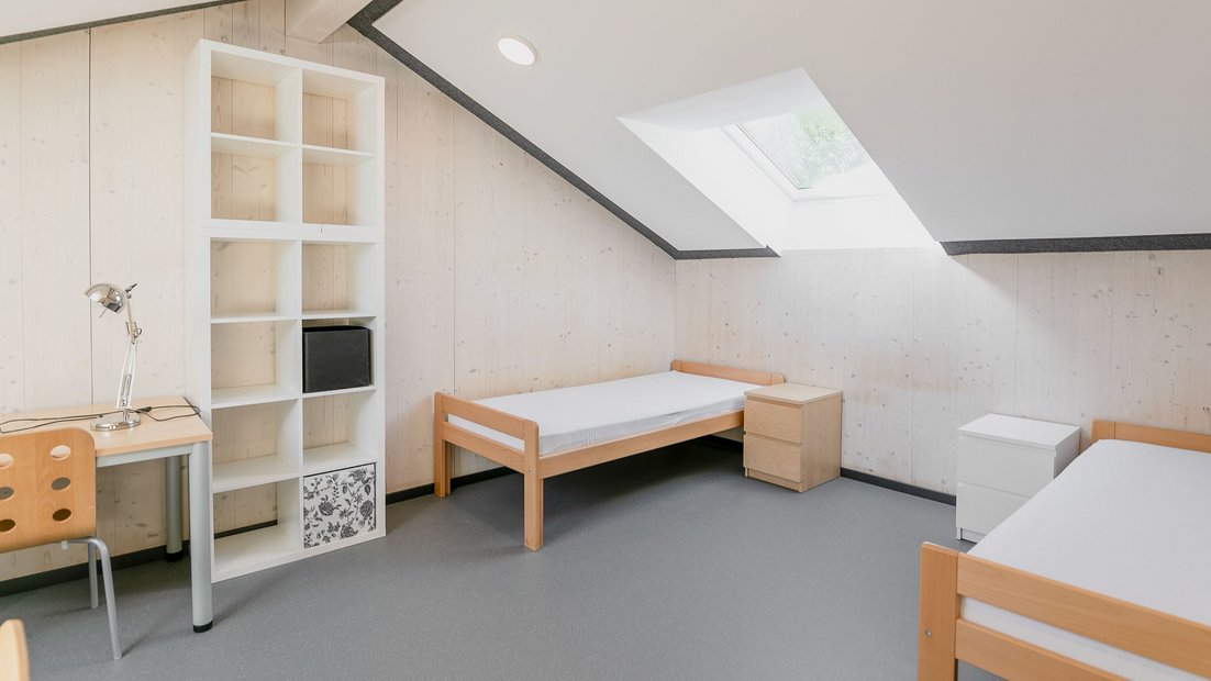 Phòng gác mái trong Rosenhaus với hai giường, kệ trắng và bàn làm việc
